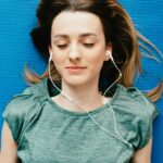 Young woman lying on yoga mat with earphones, eyes closed in relaxation.