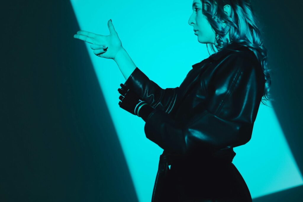 Side view of a woman in a leather coat making a hand gesture, captured in blue lighting.