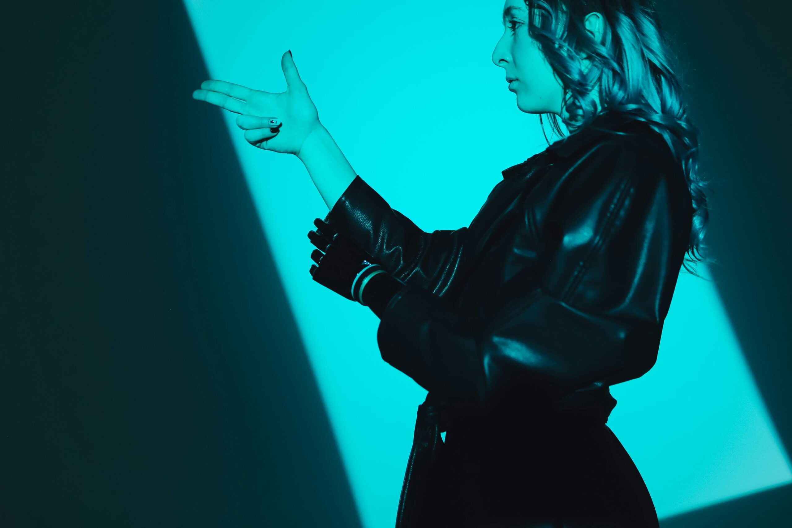 Side view of a woman in a leather coat making a hand gesture, captured in blue lighting.