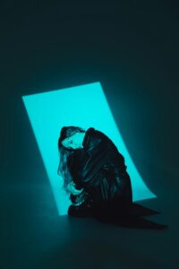 Moody portrait of a woman in black leather against dramatic turquoise lighting.