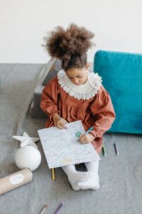 A young girl attentively colors a page while sitting on a soft surface, showcasing creativity and concentration.