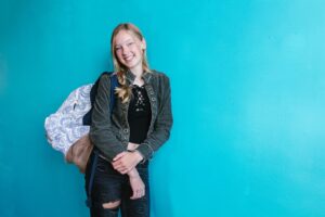 Smiling young woman posing with a stylish backpack in front of a vibrant blue background.