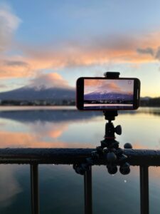 Smartphone capturing Mt. Fuji's reflection in Lake Kawaguchi during a scenic sunset.