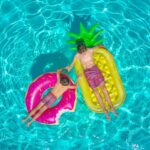Two boys relaxing on colorful inflatable floats in a swimming pool under the summer sun.