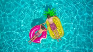 Two boys relaxing on colorful inflatable floats in a swimming pool under the summer sun.