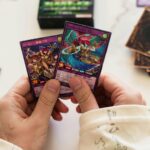 Hands holding Yu-Gi-Oh! trading cards in a dynamic gaming setup with blurred background.