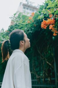 Side profile view of a woman admiring orange blossoms against a lush green backdrop, representing nature's beauty.