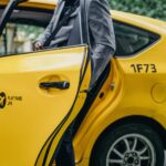 A well-dressed man in a suit exiting a yellow taxi in a city environment.