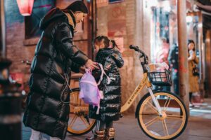 A mother helping her daughter with a backpack on a vibrant Beijing street at night.