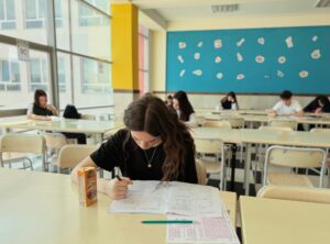 Student concentrated on exam in classroom setting with natural light.
