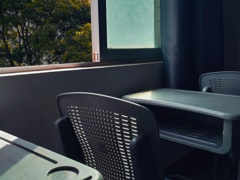 An empty classroom with desks and chairs bathed in sunlight through a window.