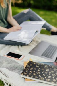 A student studies with a laptop and books on a sunny day outdoors.