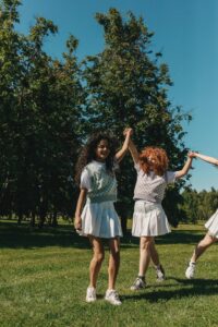 Happy teenage girls playing and holding hands in a sunny park, enjoying the outdoors.