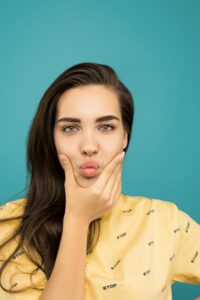 Close-up of a woman posing playfully in a yellow T-shirt against a blue background.
