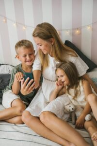 A mother and her two children are happily sitting together indoors, sharing a moment with a smartphone.