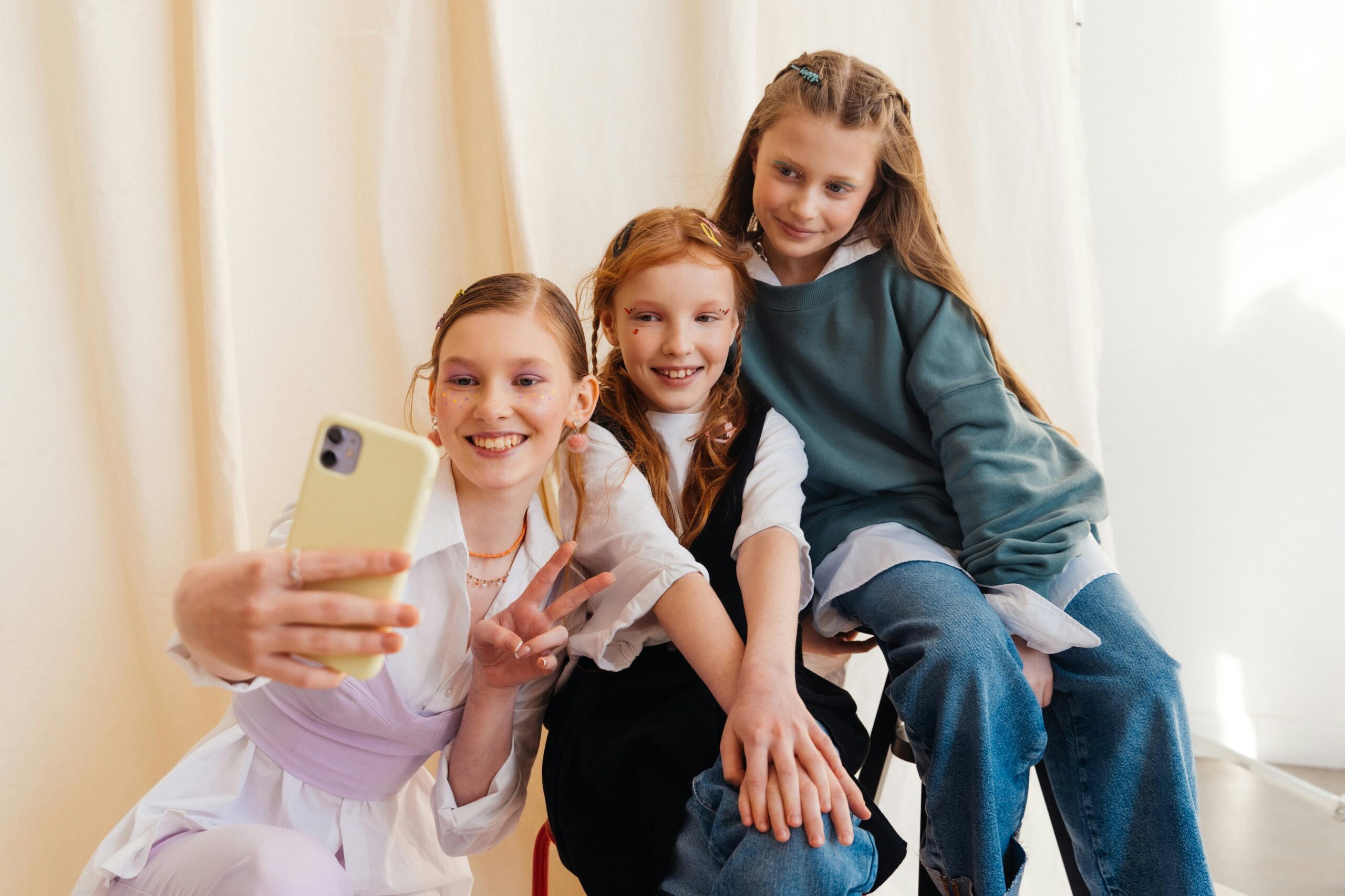 Three teenage girls smiling while taking a selfie together indoors.