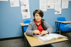 Young student sitting confidently at a desk in a classroom with books.