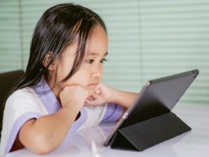 A young girl intensely focused on a tablet indoors, depicting concentration.