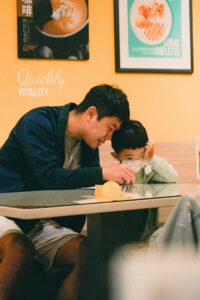 A father and son sitting at a café table, engaging and bonding over a snack.