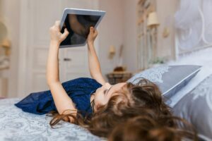 Young girl enjoys leisure time on bed with tablet, indoors.