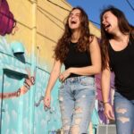 Two women laughing and enjoying a sunny day by a vibrant street mural.