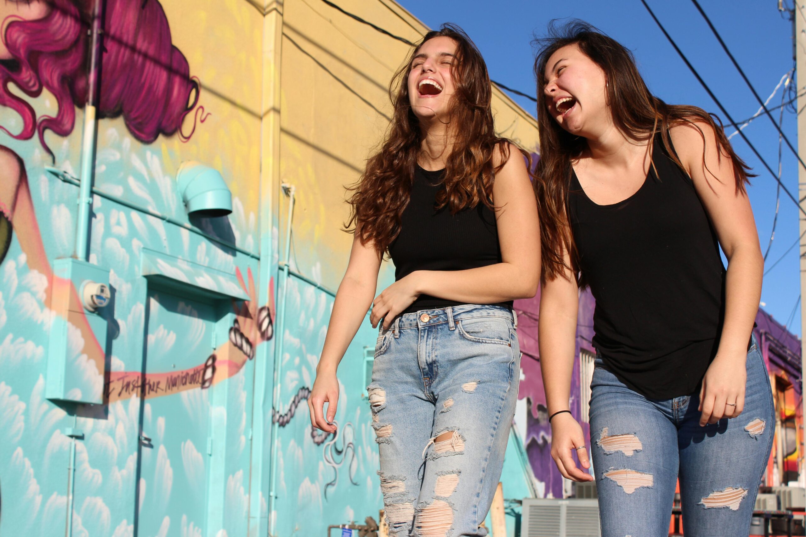 Two women laughing and enjoying a sunny day by a vibrant street mural.