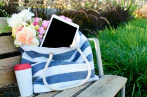 A tablet in a striped tote bag with flowers on a park bench, ideal modern outdoor scene.