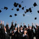 Group of graduates celebrating by throwing caps in the air during a sunny day.
