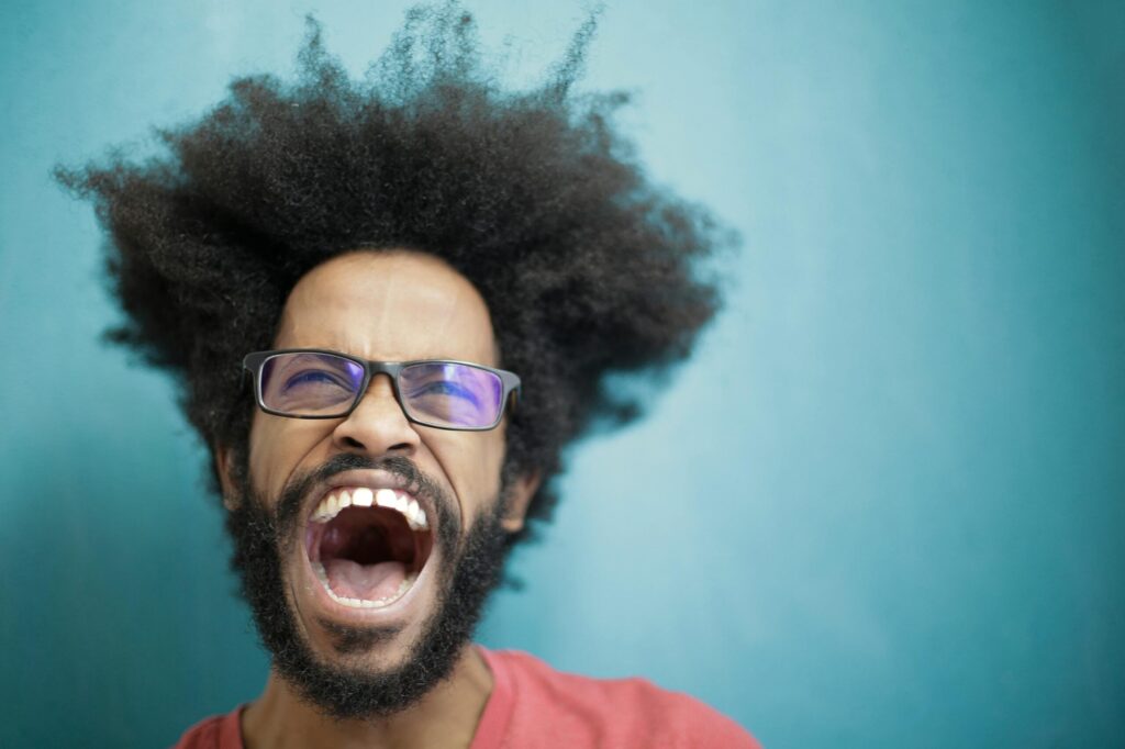 Dynamic portrait capturing a man with afro hair and eyeglasses shouting energetically in studio setting.