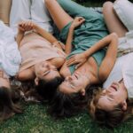 Four women laughing together while lying on the grass, embodying friendship and joy.