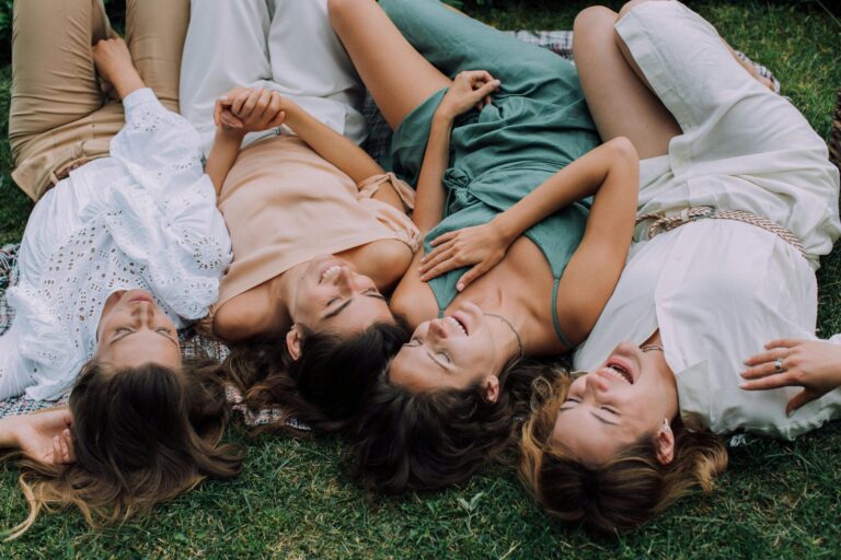 Four women laughing together while lying on the grass, embodying friendship and joy.