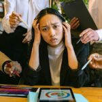 Stressed Asian businesswoman surrounded by demanding colleagues in a busy office setting.