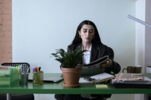 A professional woman reading a newspaper at her desk in a contemporary office setting.