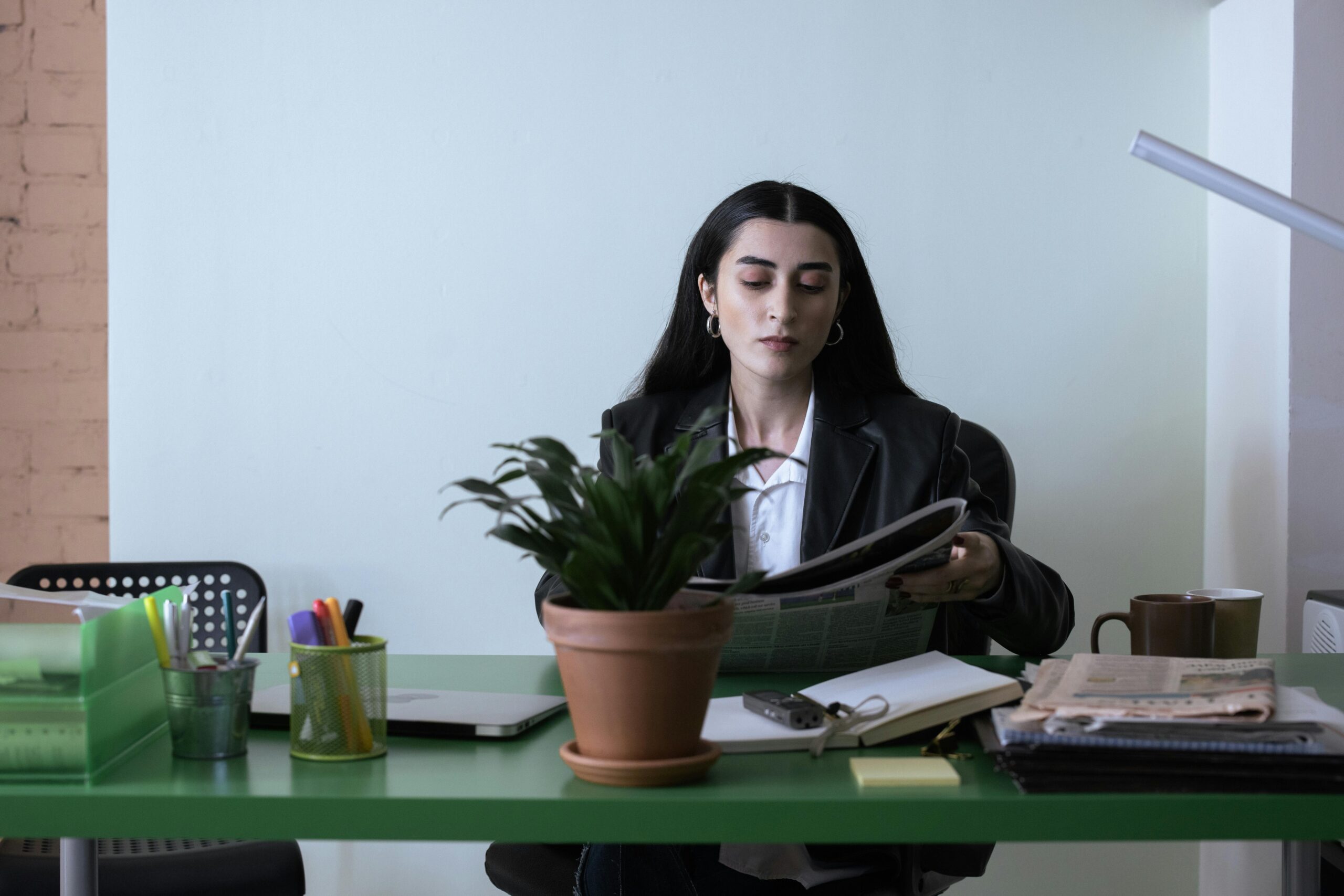 A professional woman reading a newspaper at her desk in a contemporary office setting.