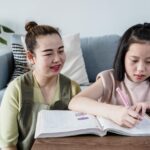 Asian mother and daughter bonding while studying on the couch in living room.