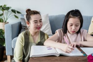 Asian mother and daughter bonding while studying on the couch in living room.