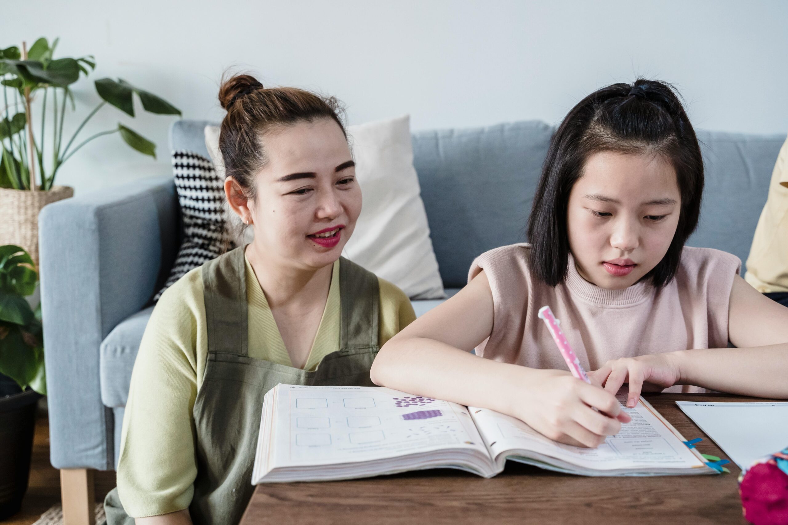 Asian mother and daughter bonding while studying on the couch in living room.