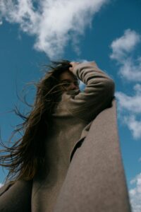 Low-angle shot of a woman with long hair in a brown coat looking over her shoulder against a bright sky.