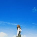 A young woman poses stylishly under a vibrant blue sky, embodying youthful fashion and freedom.