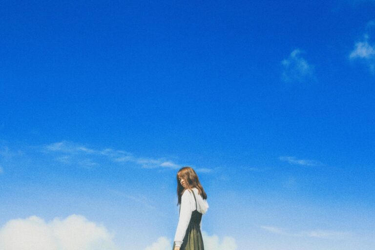 A young woman poses stylishly under a vibrant blue sky, embodying youthful fashion and freedom.