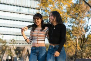 Two friends enjoy a warm autumn day outdoors, laughing and walking side by side.