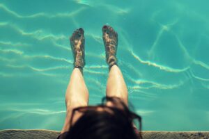 Woman relaxing with feet dipped in a clear pool on a sunny day, capturing a refreshing moment.