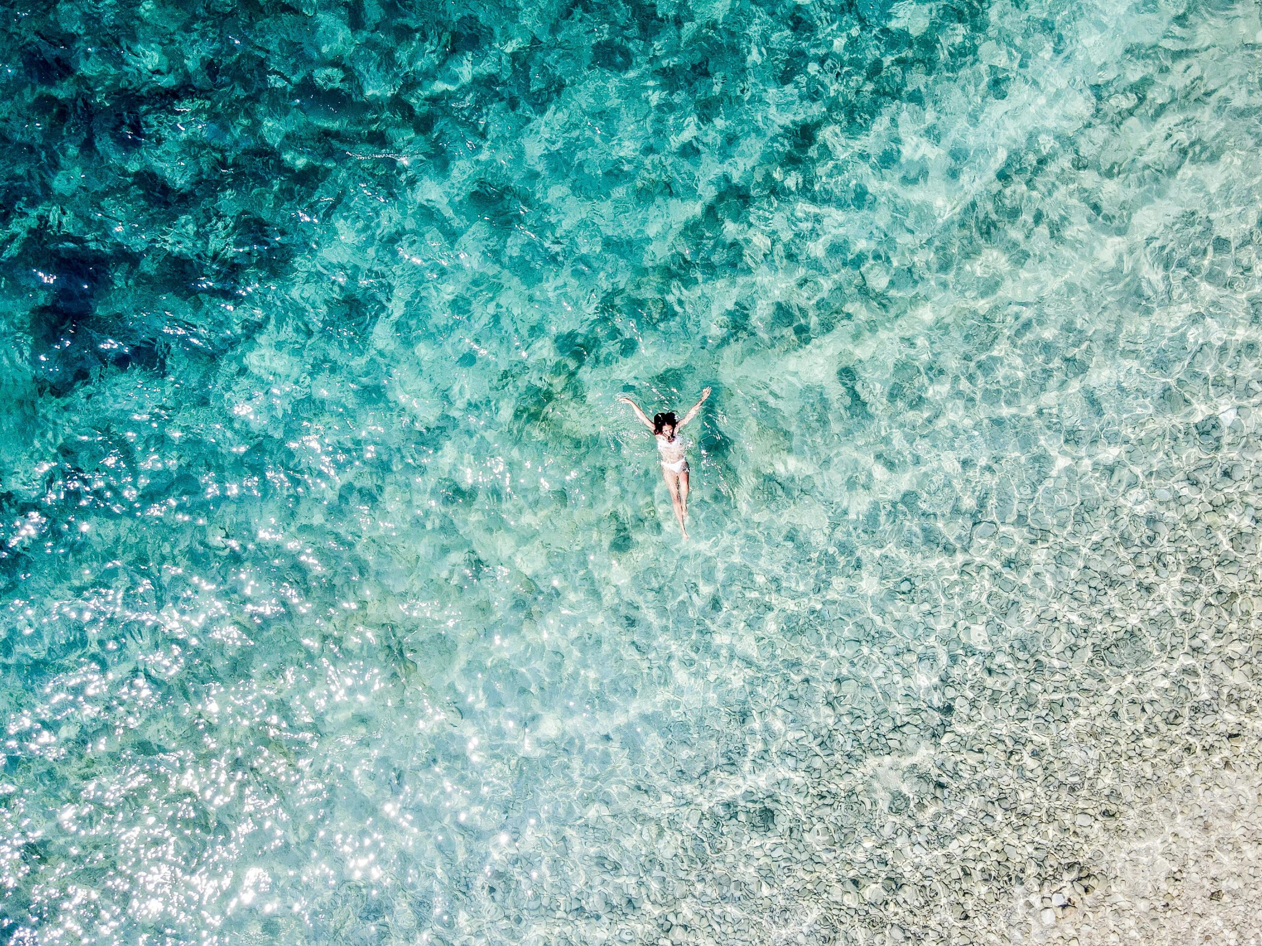 Drone shot of a woman swimming in clear blue sea off the coast of Croatia.