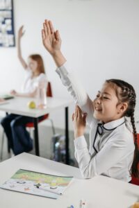 Two students actively participate in classroom with hands raised, eager to answer.
