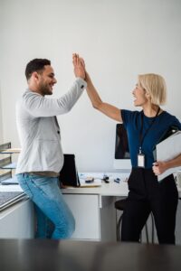 オフィスで、成功を祝ってハイタッチを交わす二人の同僚。