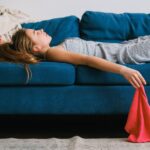 Side view of young exhausted woman with rag lying on couch in living room in daylight