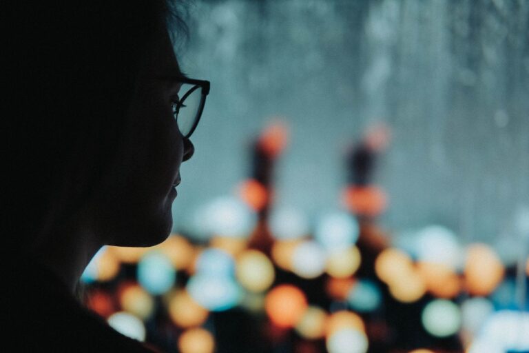 Silhouette of a woman with glasses against a bokeh light background, creating an artistic mood.