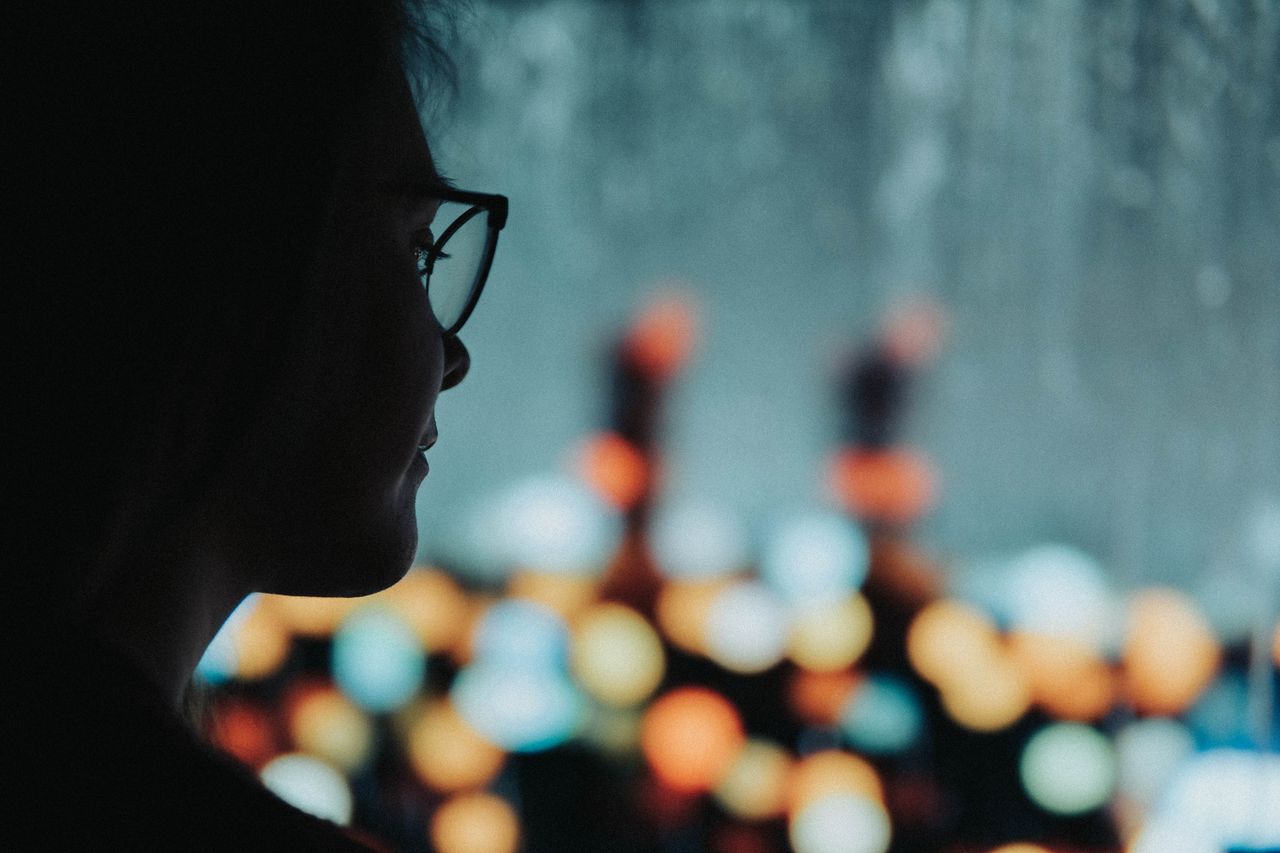 Silhouette of a woman with glasses against a bokeh light background, creating an artistic mood.