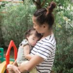 A woman holds a baby in an outdoor garden, conveying warmth and care.