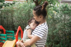 A woman holds a baby in an outdoor garden, conveying warmth and care.